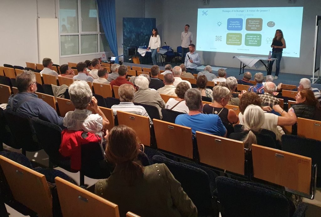 40 personnes de dos dans un amphithéâtre qui regarde une personne qui parle au micro